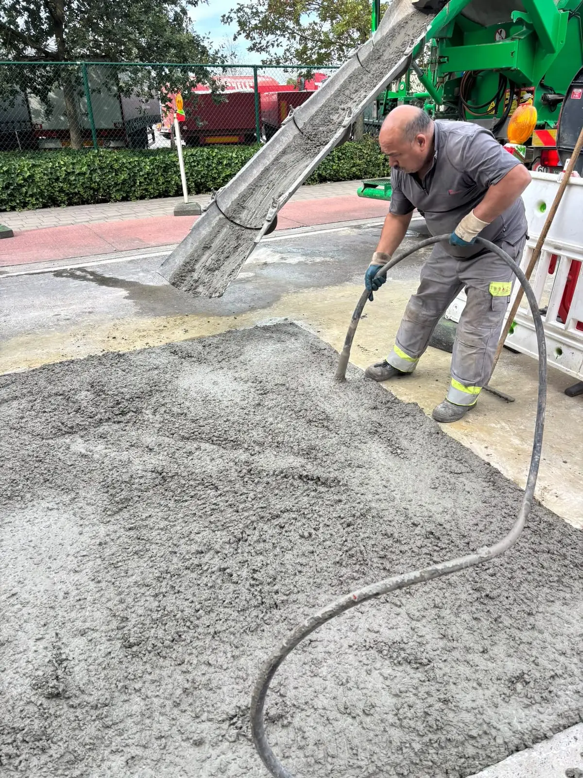 Zaakvoerder van Öz Rioleringswerken stort beton voor het voetpad in Wondelgem