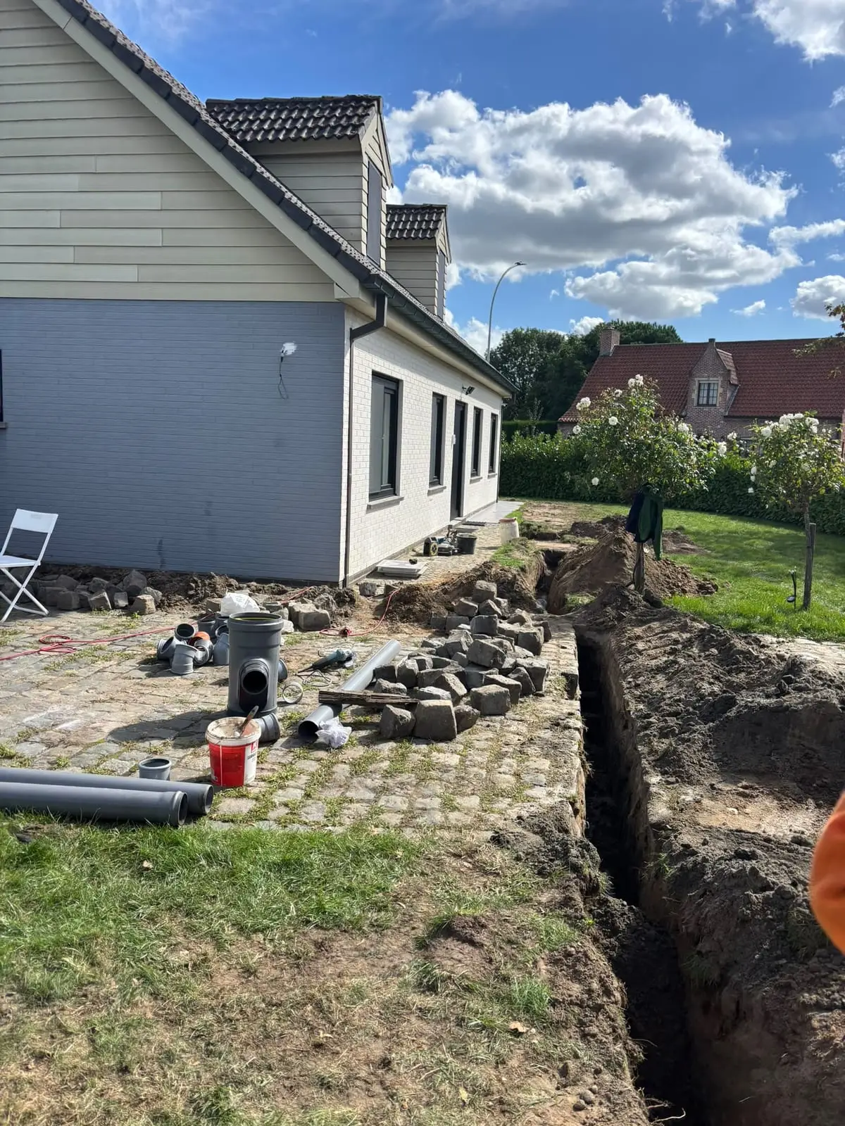 Sleuf door de tuin naast het terras voor een nieuwe afvoerleiding in Mariakerke